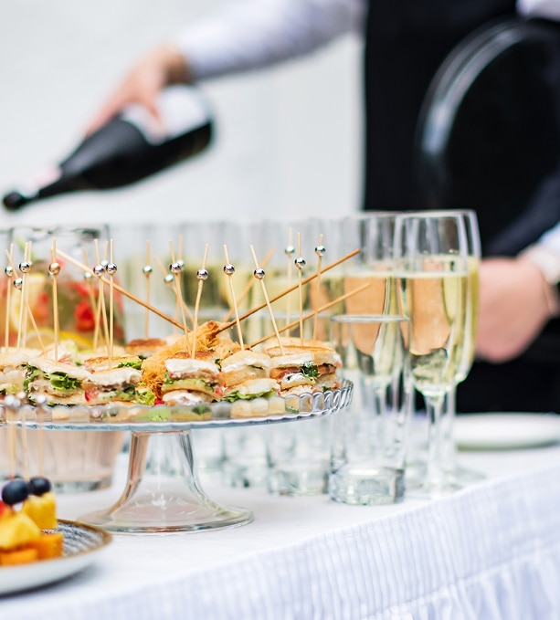 Canapés et Champagne : service traiteur élégant pour réception. Plateau de canapés sandwichs sur pied en verre. Un traiteur verse du champagne dans des flûtes lors d'un service de réception.