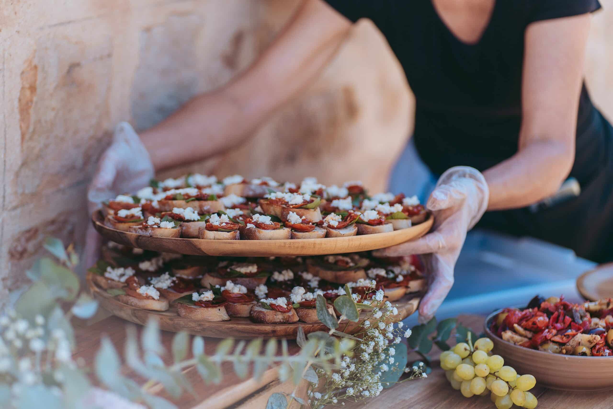 Présentation de canapés gourmet aux tomates séchées et feta sur des plateaux boisés, servis par un traiteur en extérieur.